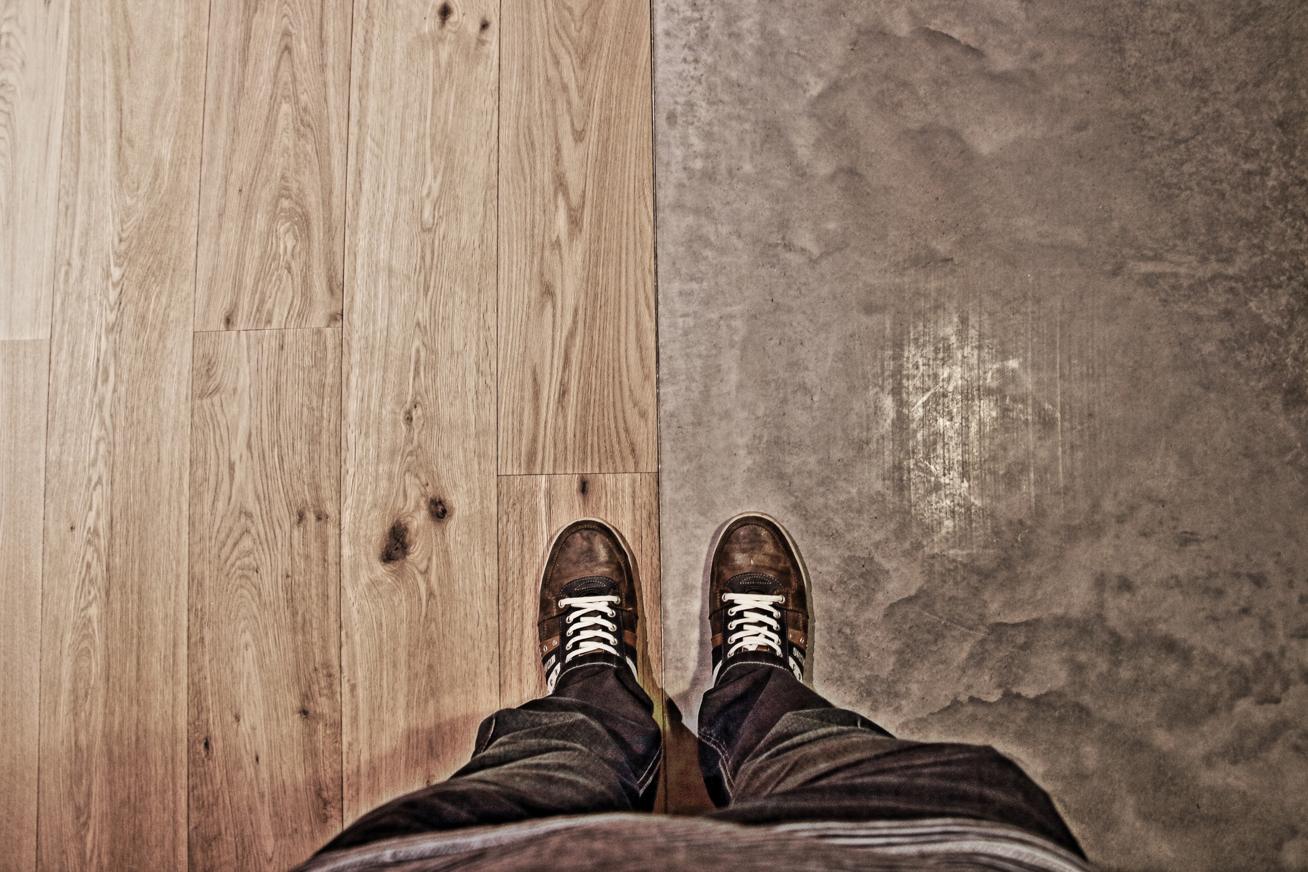 Deux chaussures placées l'une sur un sol en parquet, l'autre sur un sol en beton lissé